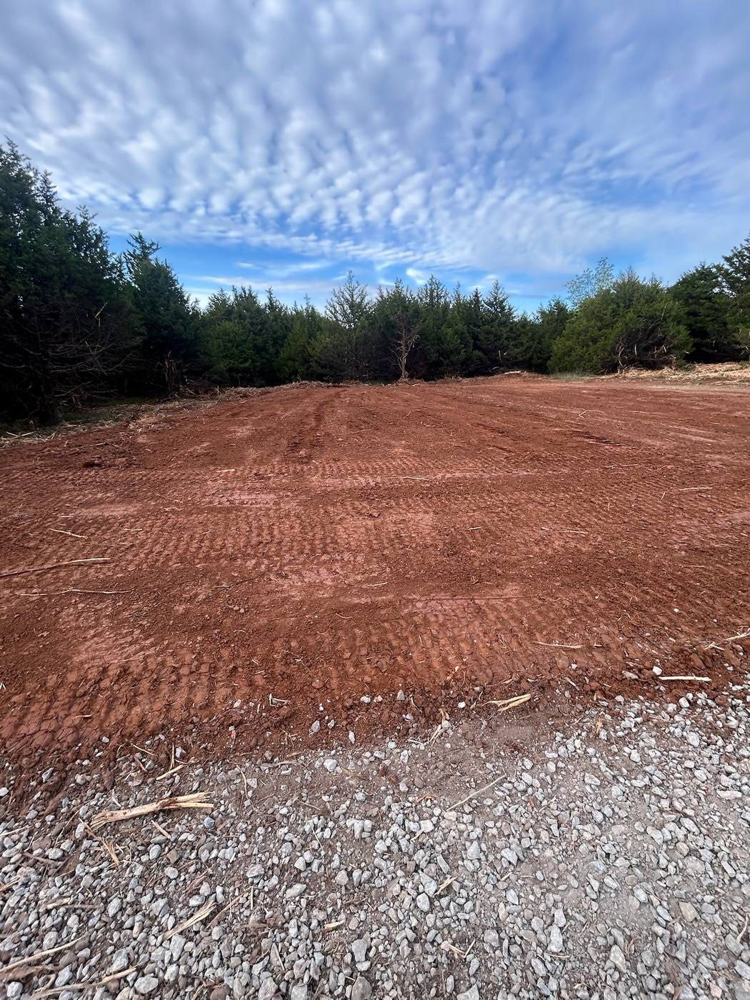 Forestry mulching results in Haskell County, Oklahoma - graded red dirt with eastern redcedar windrow at the tree line after cedar removal