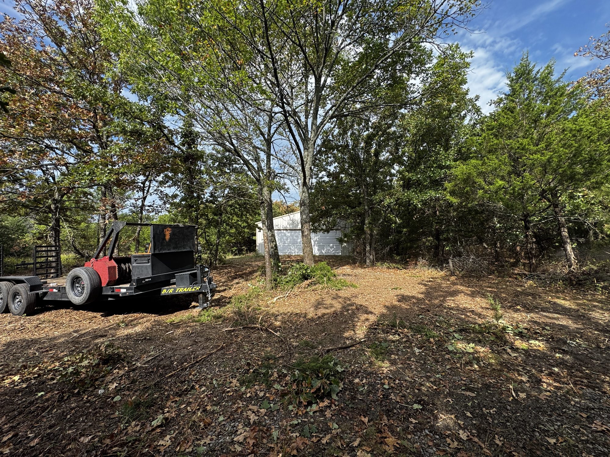 Overgrown brush and dead fall crowding a shop building before forestry mulching in Sand Springs, Tulsa County, Oklahoma